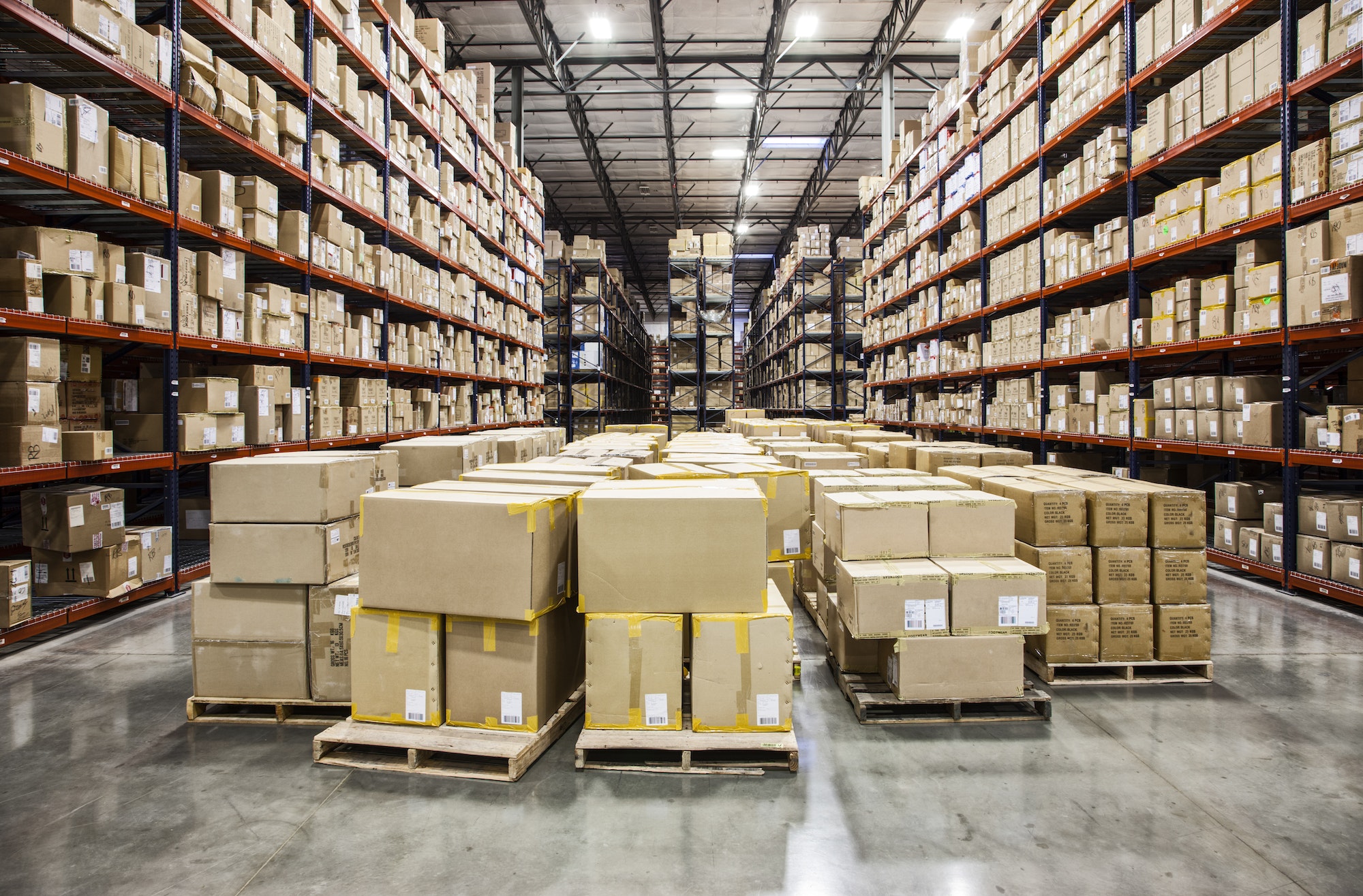View down aisles of racks holding cardboard boxes of product on pallets in a large distribution